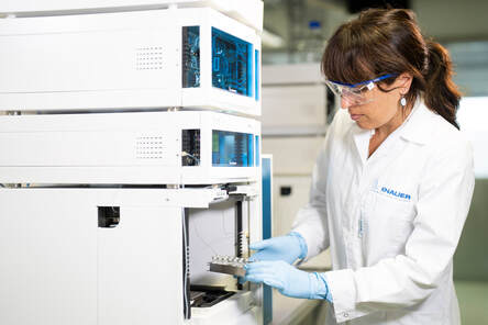 scientist wearing blue gloves and safety goggles viewing something in a lab