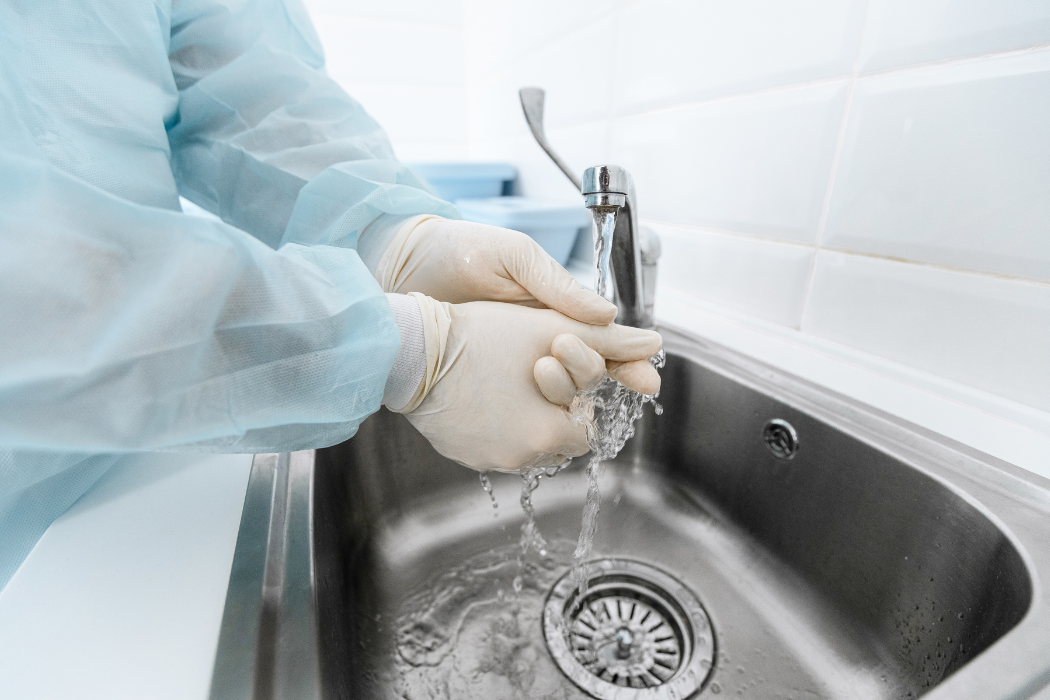 sink in a lab setting, water running from a faucet. Hands in white gloves